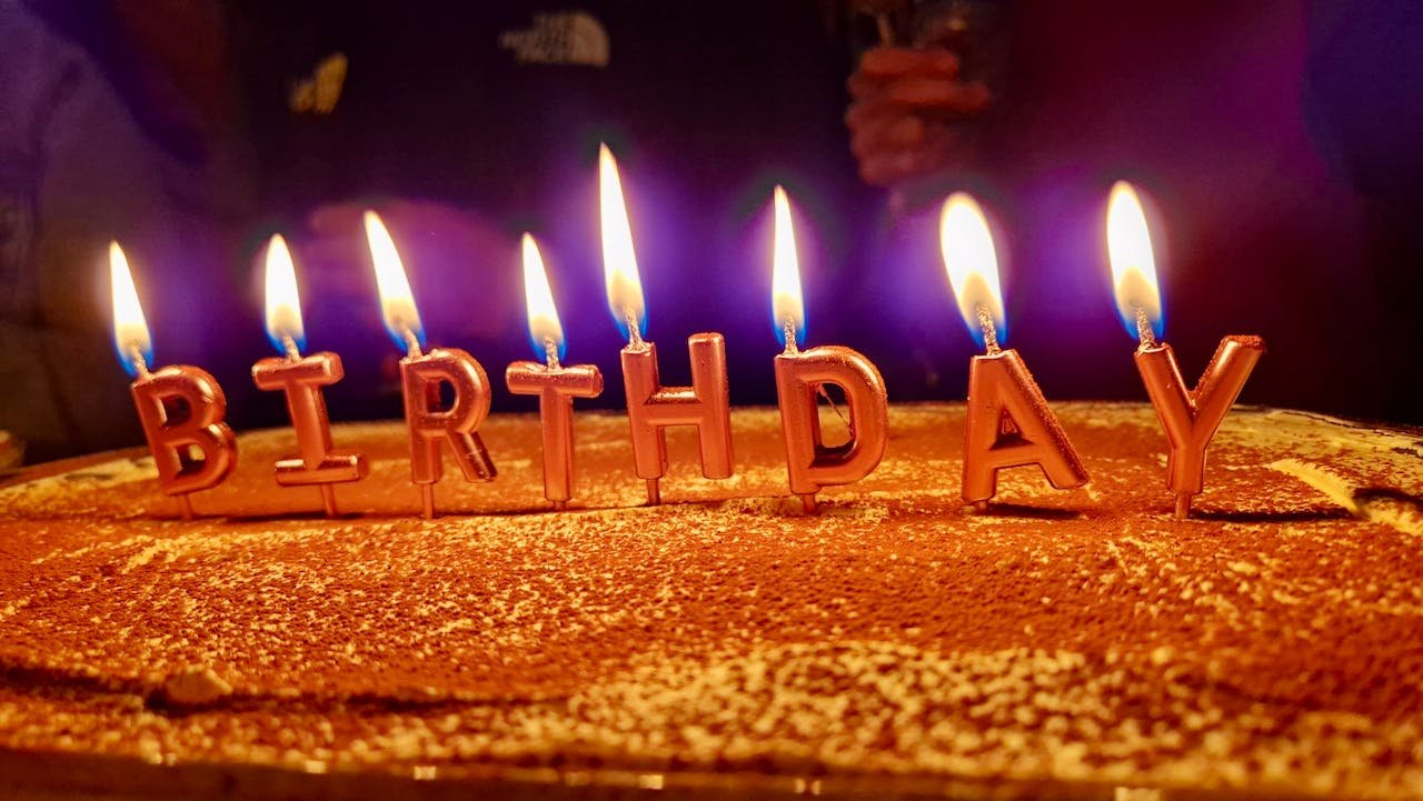 Close-up of a birthday cake with candles spelling out 'birthday' glowing warmly.